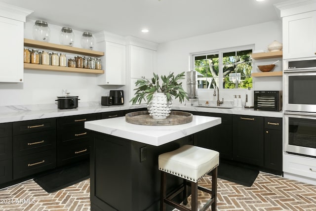 kitchen with sink, white cabinetry, a kitchen bar, a kitchen island, and stainless steel double oven