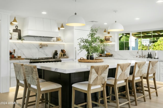 kitchen with tasteful backsplash, white cabinets, hanging light fixtures, custom range hood, and a spacious island