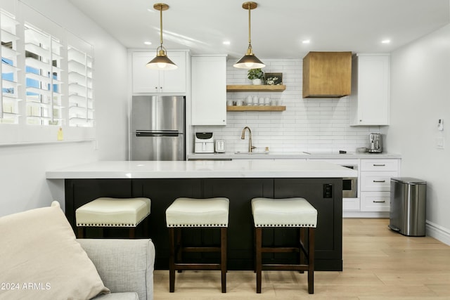 kitchen featuring pendant lighting, stainless steel fridge, a breakfast bar area, white cabinetry, and decorative backsplash