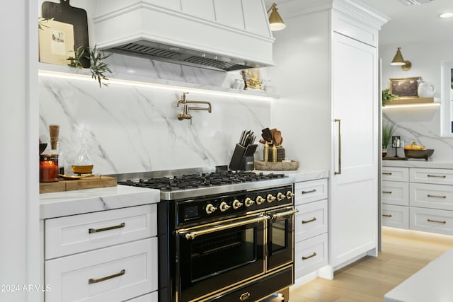 kitchen with range with two ovens, tasteful backsplash, premium range hood, and white cabinets