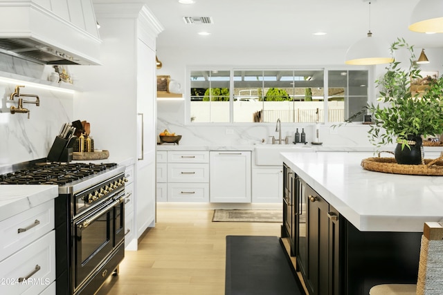 kitchen featuring premium range hood, decorative backsplash, range with two ovens, and white cabinets