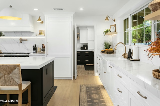 kitchen featuring sink, light hardwood / wood-style flooring, tasteful backsplash, light stone counters, and white cabinets