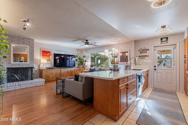 kitchen featuring sink, light hardwood / wood-style flooring, a brick fireplace, a textured ceiling, and dishwasher