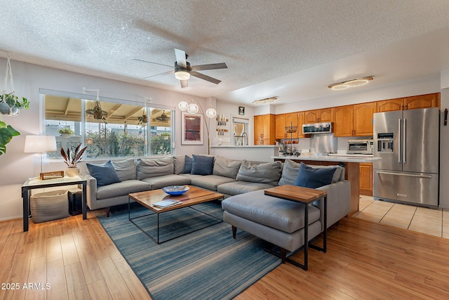 living room featuring ceiling fan, light hardwood / wood-style flooring, and a textured ceiling