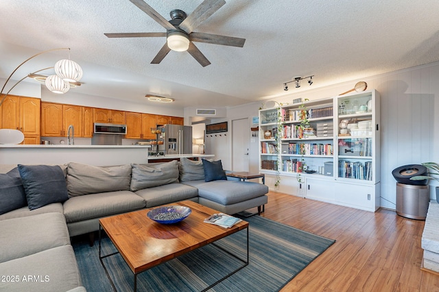 living room with ceiling fan, light hardwood / wood-style floors, and a textured ceiling