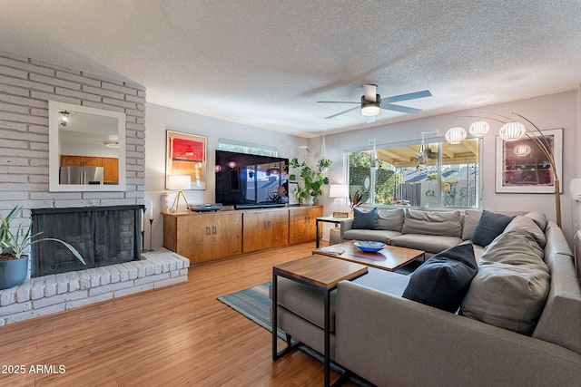 living room featuring ceiling fan, a textured ceiling, a brick fireplace, and light hardwood / wood-style flooring