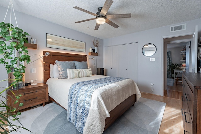 bedroom featuring ceiling fan, light hardwood / wood-style floors, a closet, and a textured ceiling