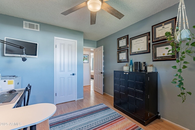 office space with a textured ceiling, ceiling fan, and light hardwood / wood-style flooring