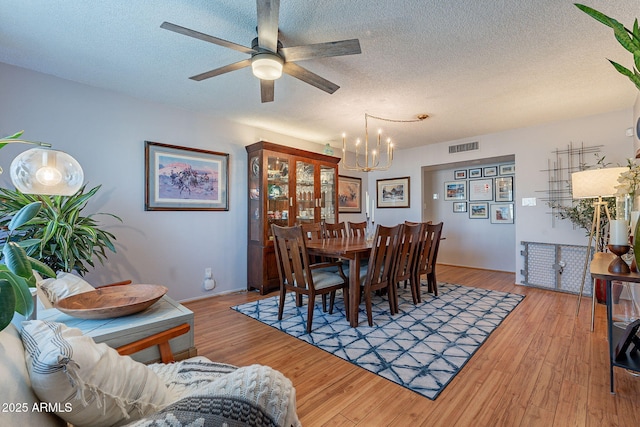 dining area featuring ceiling fan with notable chandelier, light hardwood / wood-style floors, and a textured ceiling