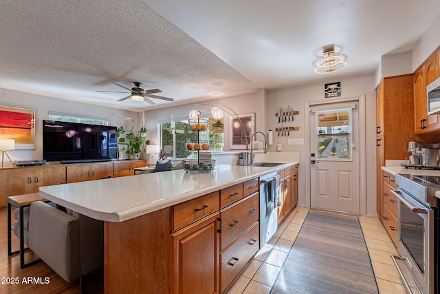 kitchen with appliances with stainless steel finishes, sink, light tile patterned floors, ceiling fan, and a textured ceiling