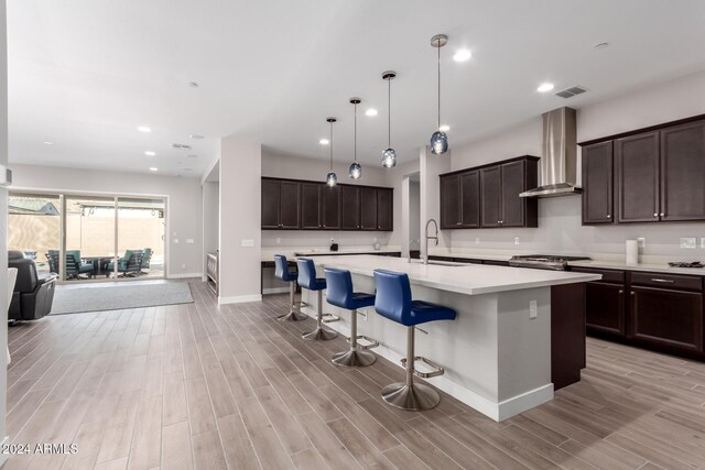 kitchen with a kitchen island with sink, sink, wall chimney range hood, and light wood-type flooring