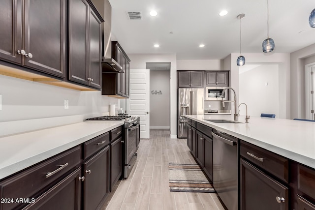 kitchen featuring dark brown cabinets, stainless steel appliances, sink, decorative light fixtures, and light hardwood / wood-style flooring