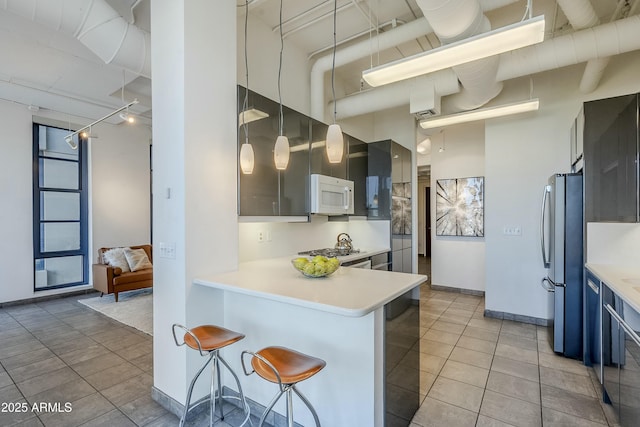 kitchen with kitchen peninsula, appliances with stainless steel finishes, a kitchen breakfast bar, and a high ceiling