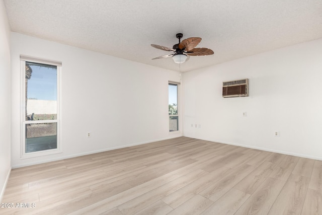 empty room with a wealth of natural light, light hardwood / wood-style flooring, a wall unit AC, and a textured ceiling