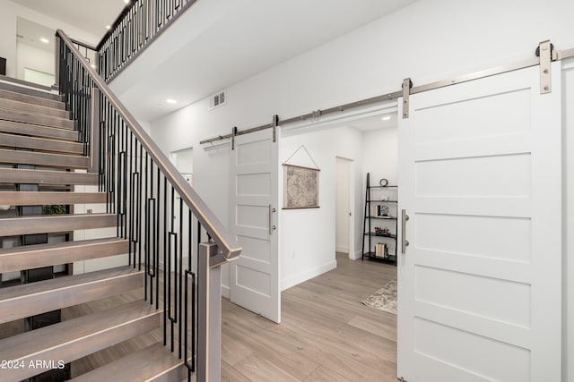 stairway with a barn door, wood finished floors, baseboards, visible vents, and recessed lighting
