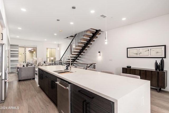 kitchen featuring light wood finished floors, a kitchen island with sink, a sink, open floor plan, and light countertops