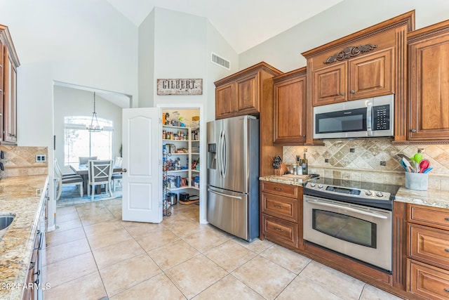 kitchen with light tile patterned flooring, light stone counters, appliances with stainless steel finishes, a notable chandelier, and decorative backsplash