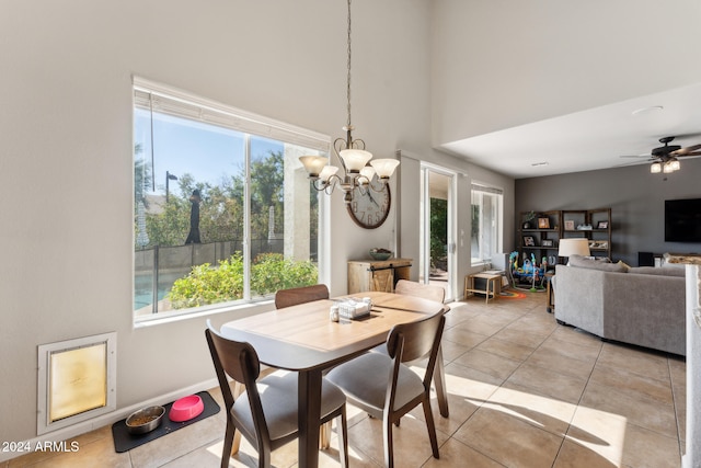 dining space with light tile patterned flooring, ceiling fan with notable chandelier, a healthy amount of sunlight, and a towering ceiling