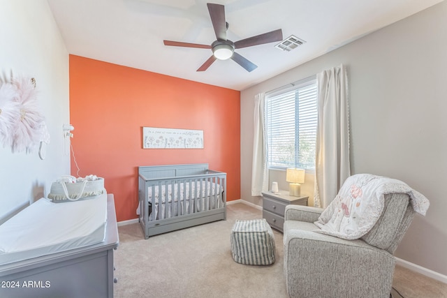 carpeted bedroom featuring ceiling fan and a crib