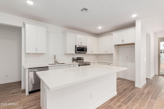 kitchen featuring white cabinets, a kitchen island, stainless steel appliances, decorative backsplash, and sink