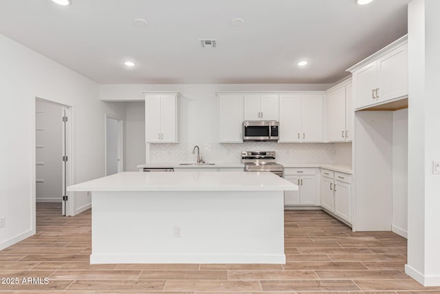 kitchen featuring backsplash, a kitchen island, light hardwood / wood-style flooring, stainless steel appliances, and white cabinets