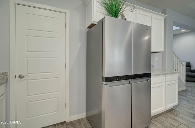 kitchen with freestanding refrigerator, light stone countertops, light wood-style flooring, white cabinets, and baseboards