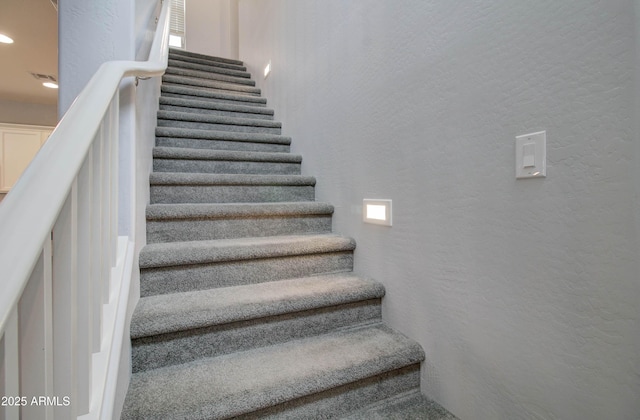 stairs with a textured wall, recessed lighting, and visible vents