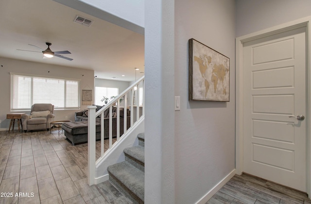stairs with wood finished floors, ceiling fan, baseboards, and visible vents