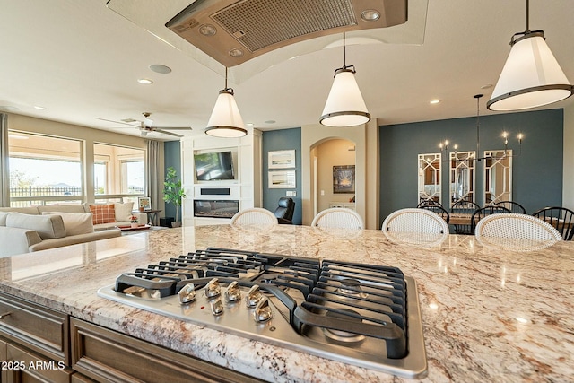 kitchen with stainless steel gas stovetop, a large fireplace, light stone counters, and decorative light fixtures