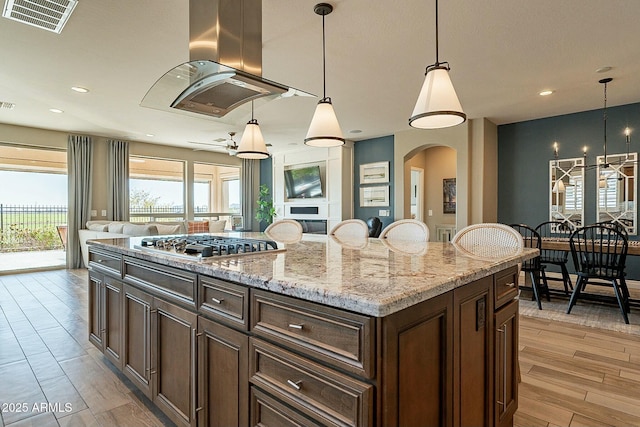 kitchen with pendant lighting, island range hood, stainless steel gas stovetop, and a kitchen island