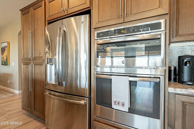 kitchen featuring stainless steel appliances, light stone countertops, and light wood-type flooring