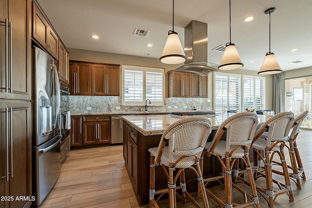 kitchen with island exhaust hood, decorative light fixtures, light stone countertops, and a kitchen island