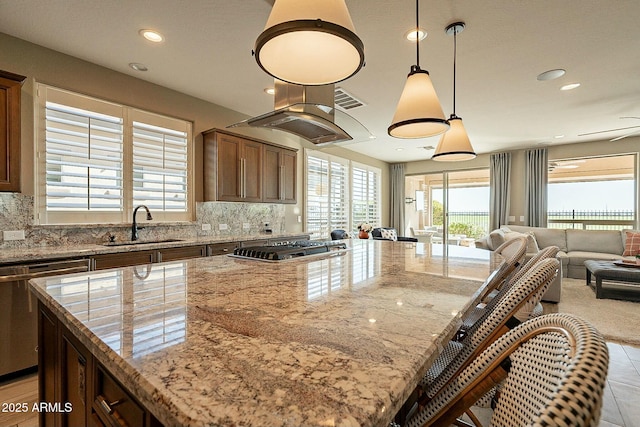 kitchen featuring decorative light fixtures, sink, a center island, light stone counters, and a healthy amount of sunlight