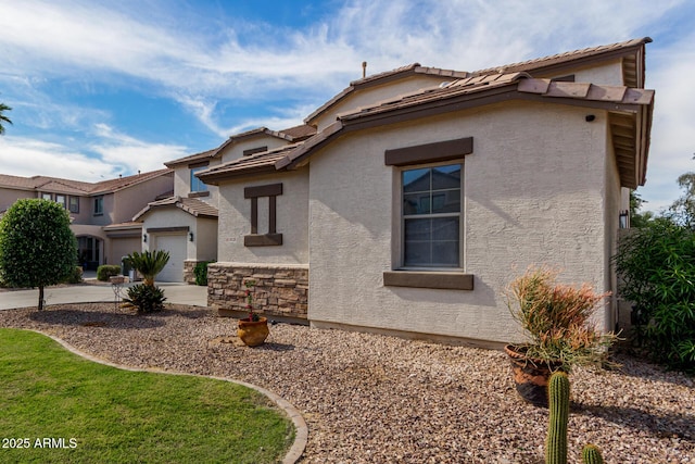 view of home's exterior with concrete driveway, stucco siding, a tile roof, stone siding, and a garage