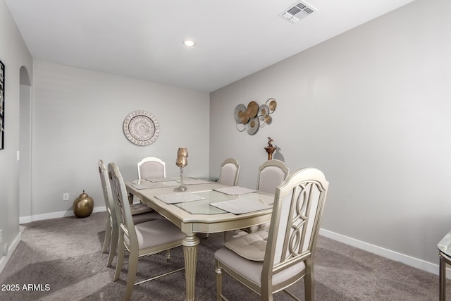 carpeted dining room featuring arched walkways, visible vents, and baseboards