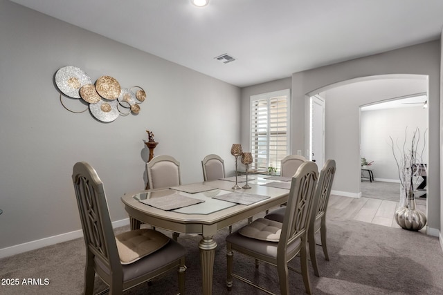 dining room featuring arched walkways, baseboards, visible vents, and light colored carpet
