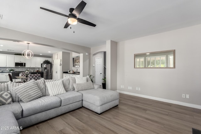 living room featuring arched walkways, wood finished floors, a ceiling fan, and baseboards