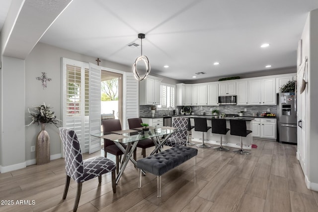 dining area with light wood finished floors, arched walkways, baseboards, and recessed lighting