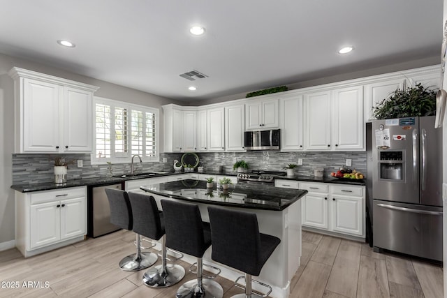 kitchen with a kitchen breakfast bar, a sink, stainless steel appliances, white cabinets, and visible vents