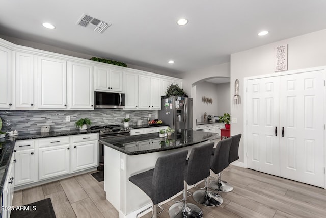 kitchen with white cabinets, arched walkways, appliances with stainless steel finishes, and visible vents