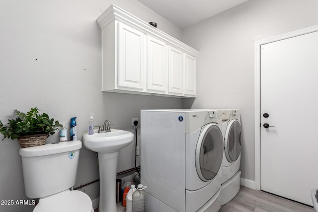 laundry area featuring washer and dryer, cabinet space, a sink, and light wood finished floors
