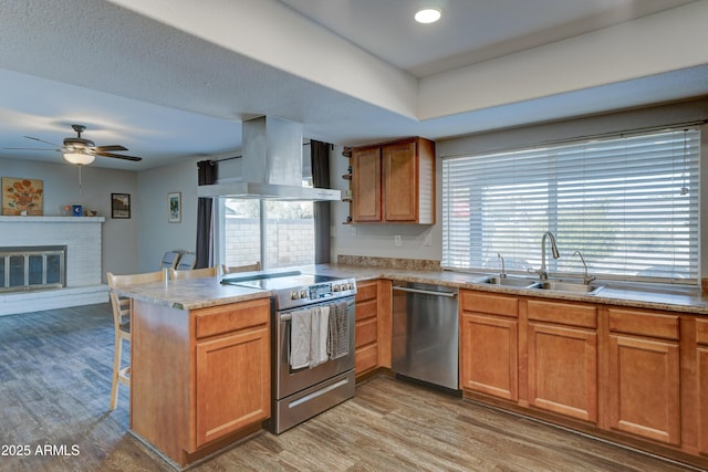 kitchen featuring appliances with stainless steel finishes, sink, kitchen peninsula, a brick fireplace, and wall chimney range hood