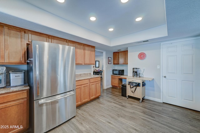 kitchen featuring built in desk, light hardwood / wood-style flooring, stainless steel refrigerator, and a raised ceiling