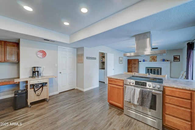 kitchen featuring island exhaust hood, a brick fireplace, electric range, and light hardwood / wood-style floors