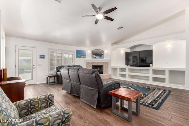 living room with visible vents, a fireplace with raised hearth, lofted ceiling, ceiling fan, and wood finished floors