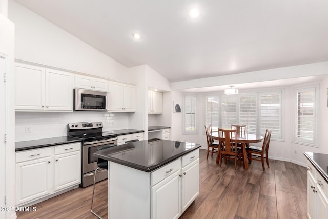 kitchen with a center island, stainless steel appliances, dark countertops, vaulted ceiling, and wood finished floors