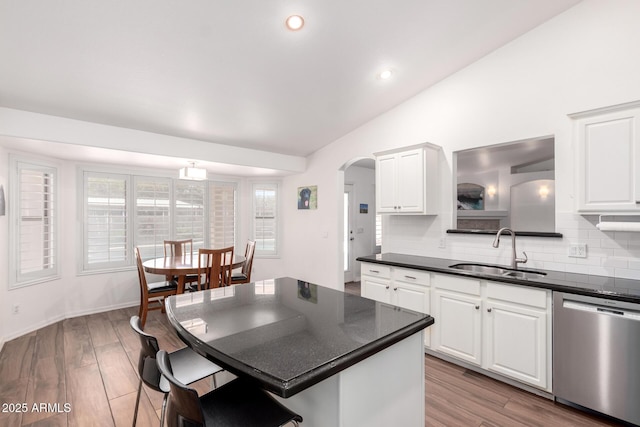 kitchen with arched walkways, dishwasher, dark countertops, vaulted ceiling, and a sink