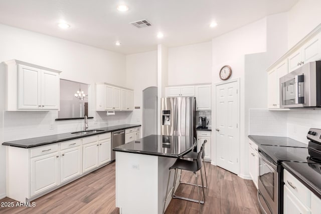 kitchen with visible vents, dark countertops, a kitchen island, appliances with stainless steel finishes, and a sink