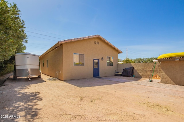 back of house with dirt driveway, fence, a patio, and stucco siding