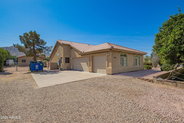 view of property exterior featuring concrete driveway, a tile roof, an attached garage, a gate, and stucco siding